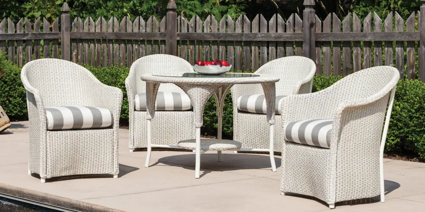 White wicker outdoor dining chairs with grey and white seat cushions near a round table